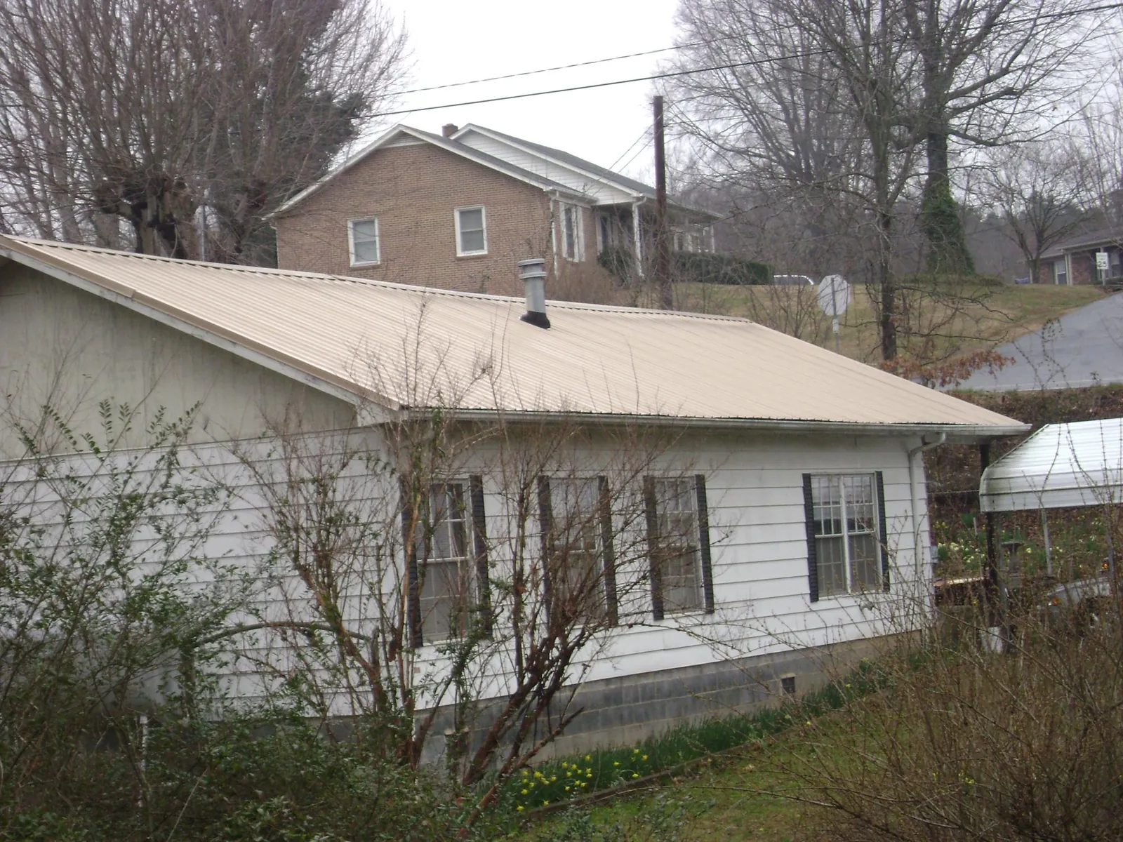 Tan metal roof on a white sided house set into a hillside — Commercial Roofing by Roofing Brothers in Hartford